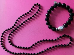 Tradera Halsband<Svart halsband och armband. Armbandet har en figur och bredvid den stenar.
